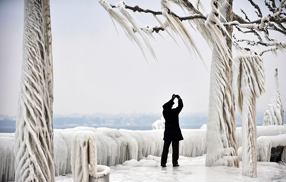 Un homme en noir prend des photos des arbres recouverts de glace au bord du lac léman durant l'hiver 2012