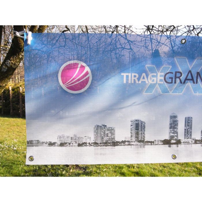 Une banderole publicitaire imprimée micro perforée mesh Tiragegrandformat est accrochée entre deux arbres