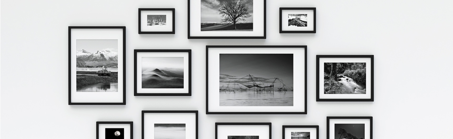 Photographie en noir et blanc de cadres photo en bois noir de différents formats portrait et paysage qui sont accrochés à un mur