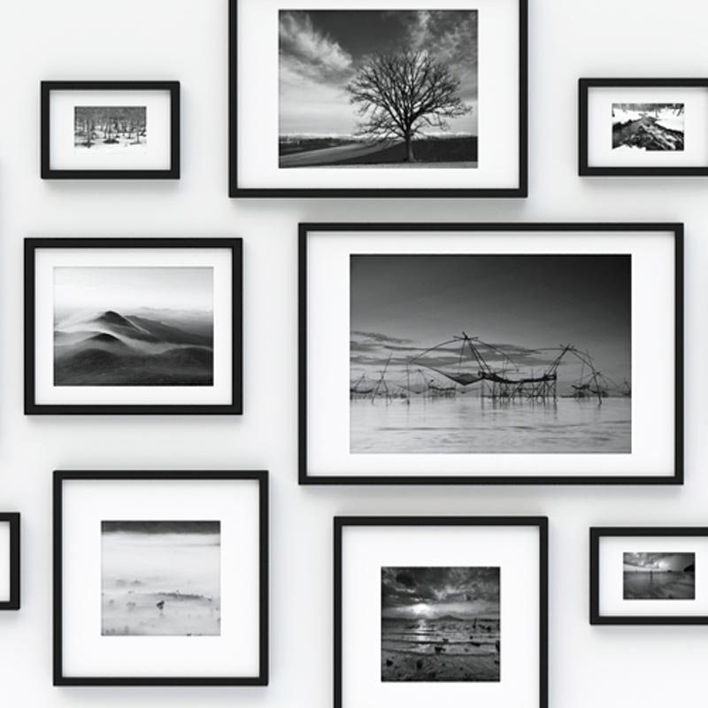 Photographie en noir et blanc de cadres photo en bois noir de différents formats portrait et paysage qui sont accrochés à un mur